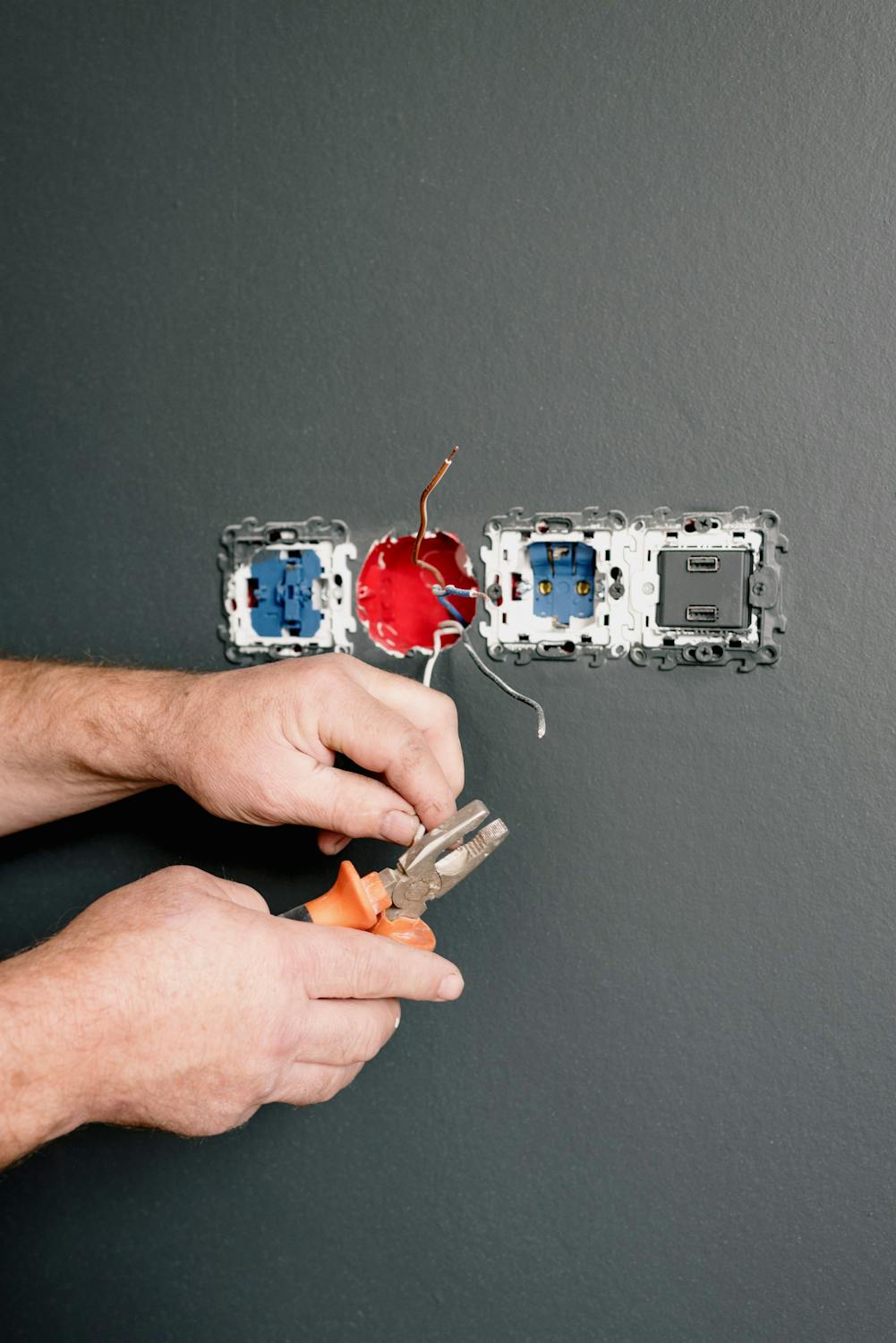 Electrician using pliers to repair electrical outlet and wiring